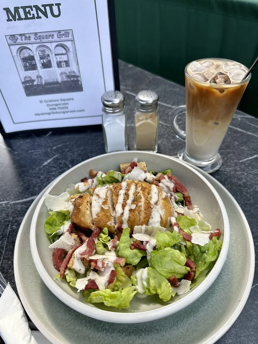 Chicken Caesar salad and an iced coffee, with The Square Grill menu behind